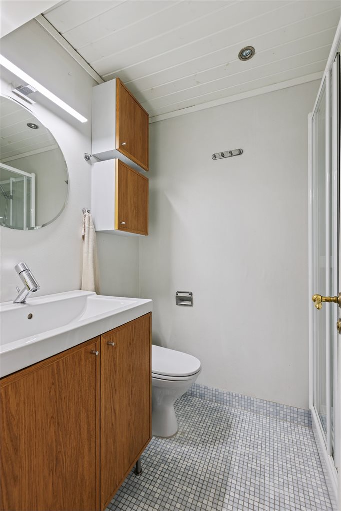 Badet i delikat utførelse med mosaikkfliser på gulv, innredet med servant, dusjkabinett og toalett. 