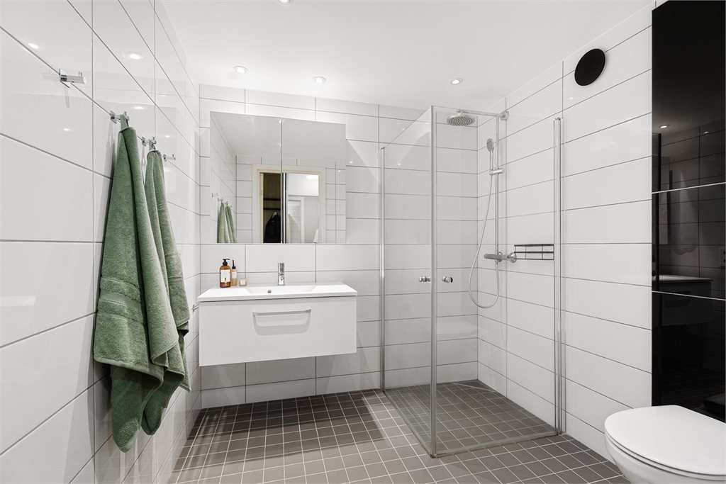 Fra gangen er det dør til flislagt baderom med tidløse overflater og praktisk innredning med oppbevaring i servant og vegghengt toalett. 