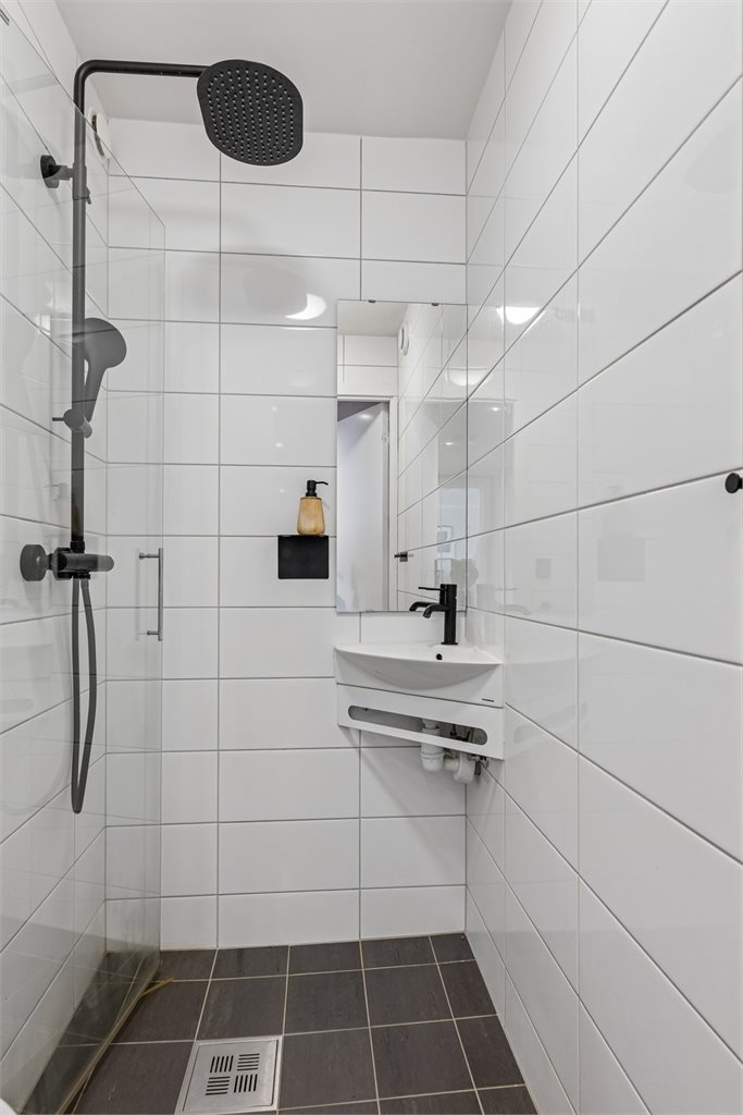 Badet er innredet med toalett, dusjdør og servant med speil. 