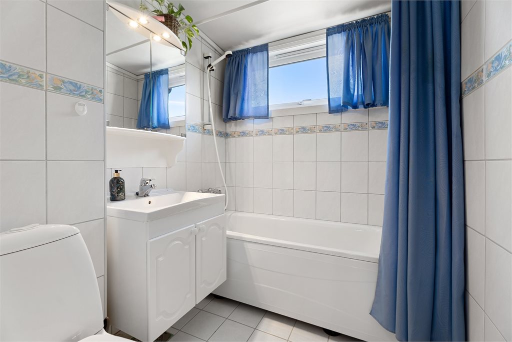 Flislagt bad med badekar, servantinnredning og vindu som gir godt lys