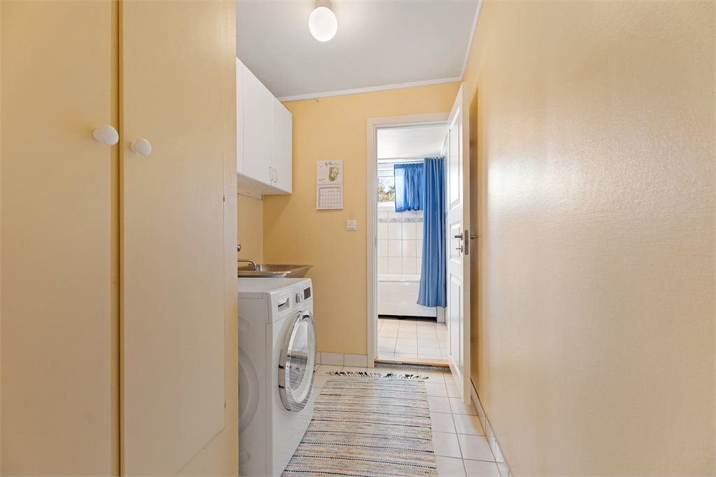 Praktisk vaskerom i tilknytning til bad, med oppbevaringsløsninger og opplegg for vaskemaskin