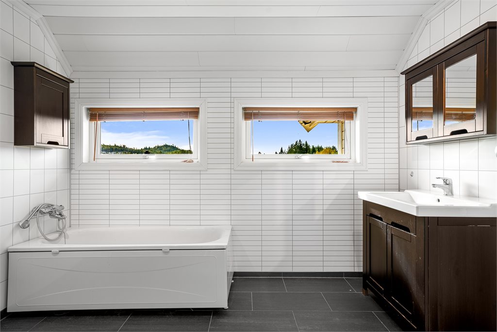 Romslig bad med badekar, servantinnredning og vinduer som sørger for godt med naturlig lys.
