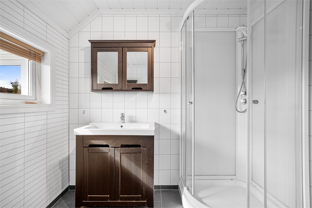 Badet er utstyrt med dusjkabinett, servant med oppbevaring og speilskap.