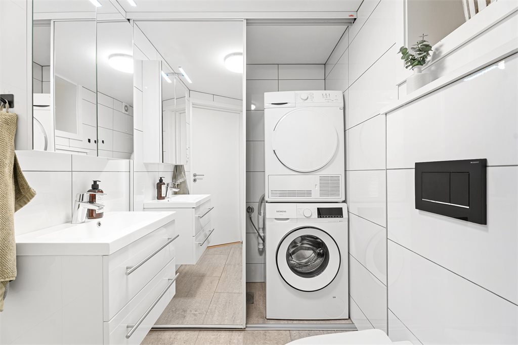 Vaskemaskin og tørketrommel er diskret skjult bak skyvedører, noe som gir et ryddig og stilrent uttrykk.
