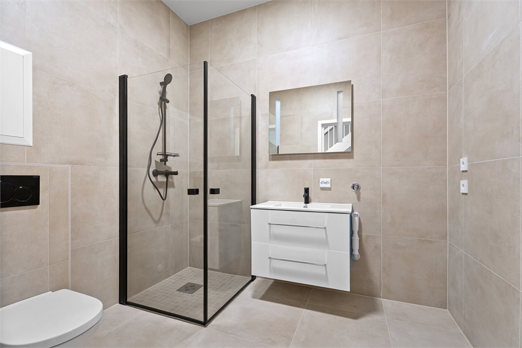 Flott flislagt bad med vegghengt toalett, dusjhjørne og innredning. Klargjort for vaskemaskin og tørketrommel.