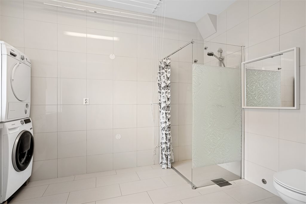 Romslig bad/vaskerom med dusj og opplegg for vaskemaskin
