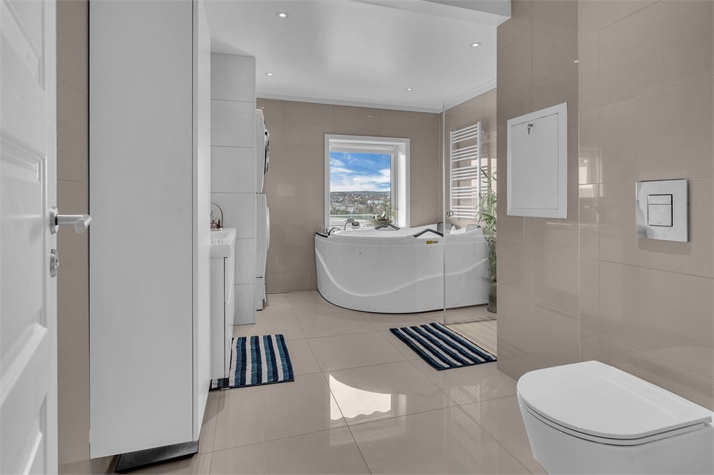 Stort flislagt bad med dusjhjørne og badekar.