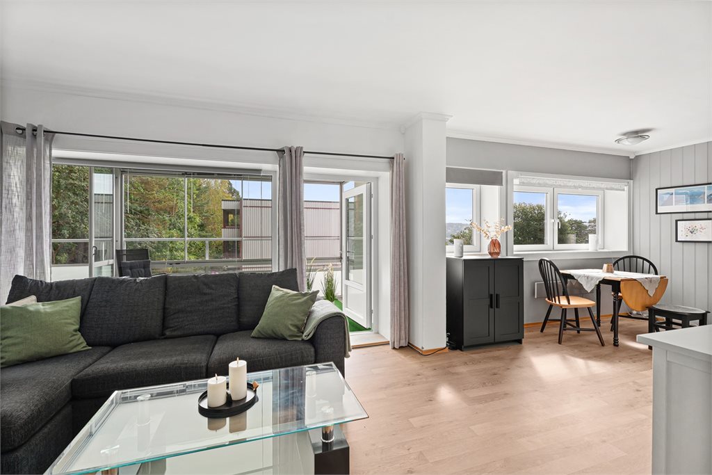 Stuen har god plass til både sofagruppe og spisegruppe, og ligger i delvis åpen løsning mot kjøkkenet. Store vindusflater og utgang til balkong bidrar til en lys og luftig atmosfære.