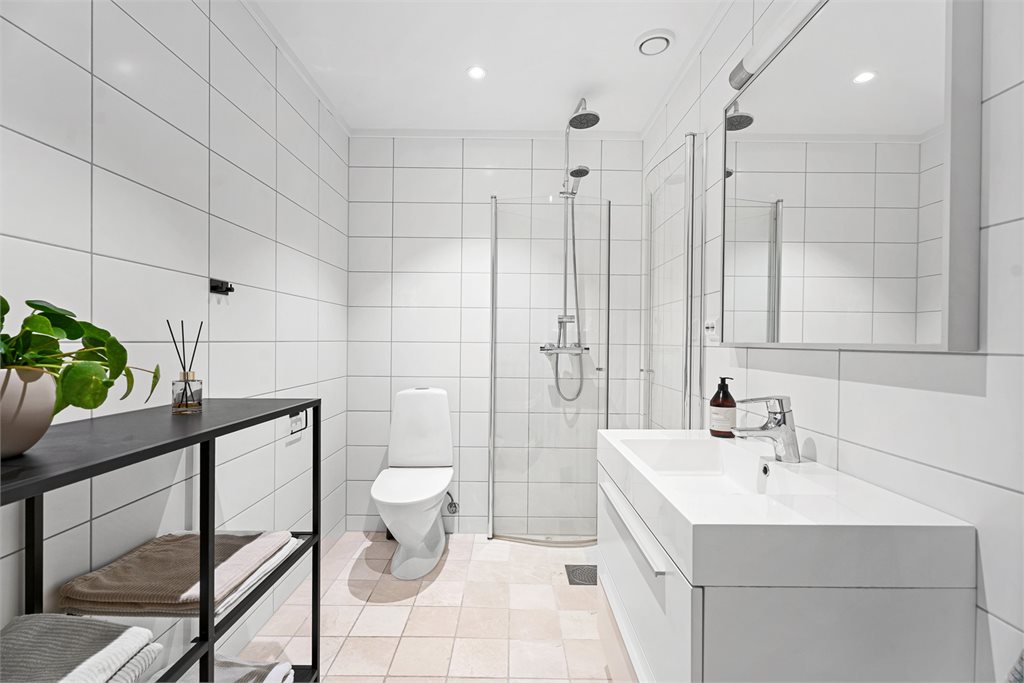 Badet har en tidløs utførelse med lyse fliser på gulv og vegger, samt downlights i himling. 