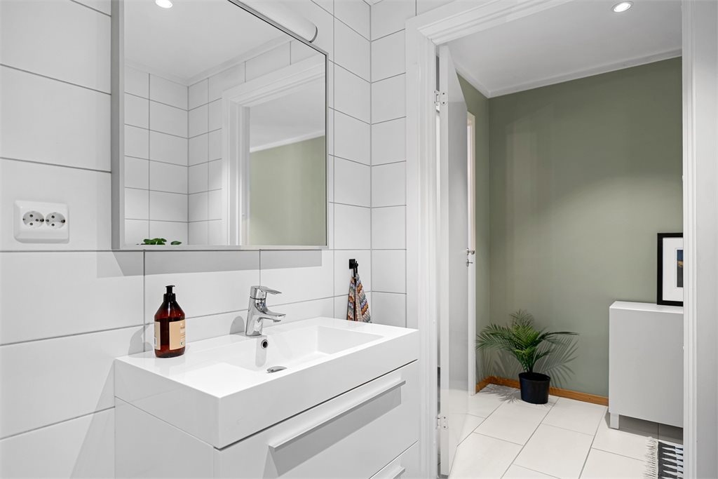 Badet er innredet med hjørnedusj, toalett og servant med speil. 