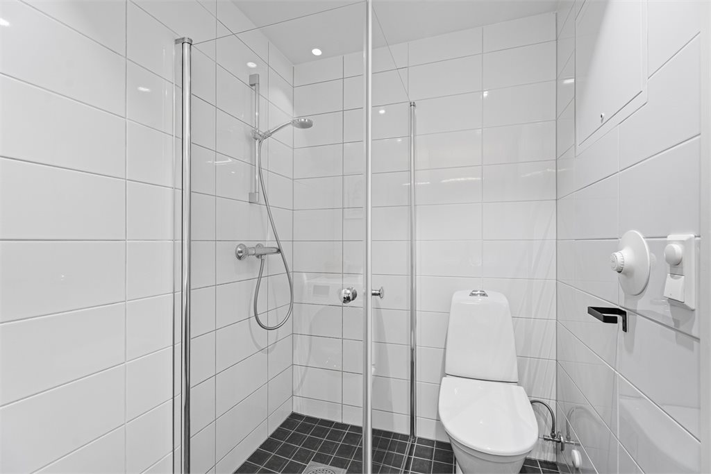 Badet er innredet med dusjhjørne, toalett og baderomsinnredning med speil og lys. 