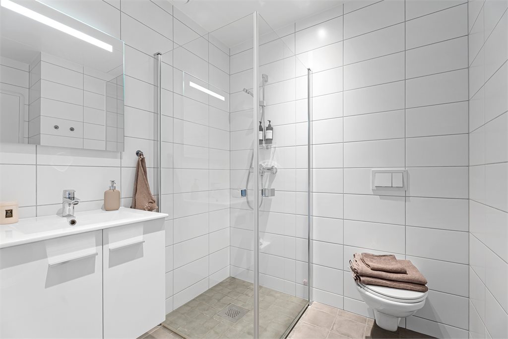 Badet er helfliset og innredet med dusjhjørne, vegghengt toalett og lekker servant.