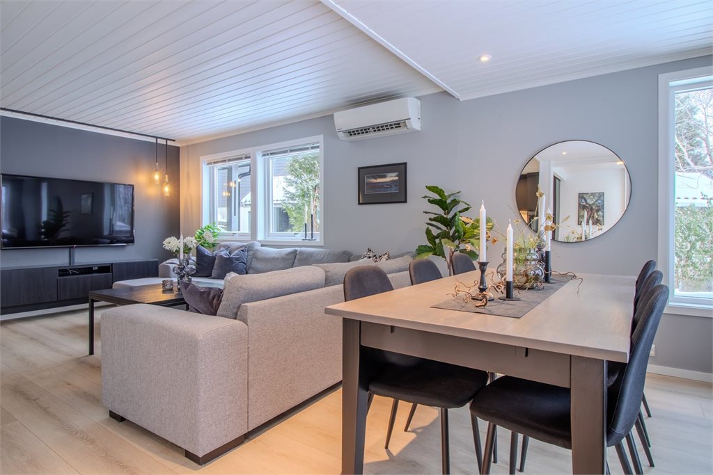 Lys og romslig stue med store vindusflater og god plass til både sofa- og spisegruppe. Varmepumpe på vegg.