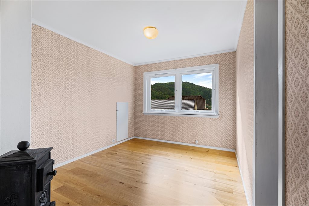 Lyst rom med parkettgulv, fint utsyn og sjarmerende vedovn.