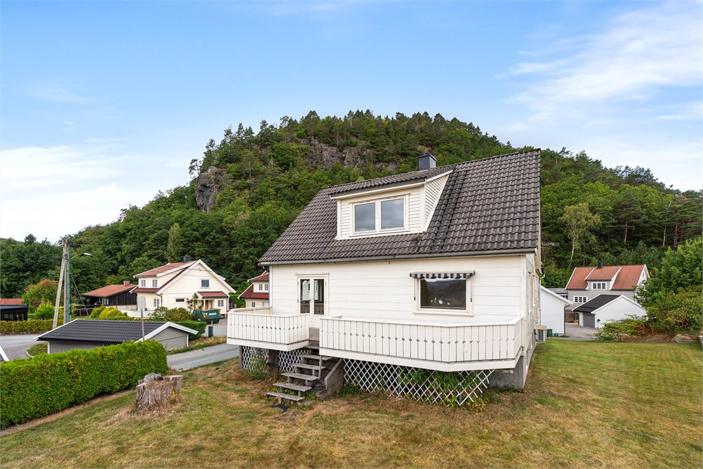 Enebolig med terrasse og hagearealer, fint plassert med grønn åsside som bakteppe.